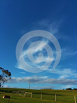 Swirly cloud floating in deep blue sky over farmland. photo