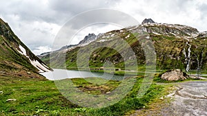 Swiss Alps mountain pass panoramic scene with lake and cloudy dramatic sky