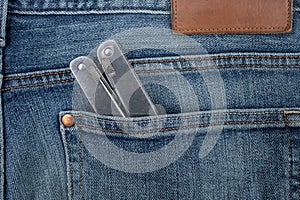 Swiss army pocket pliers in a back pocket of a pair of blue jeans, abstract backdrop, close up