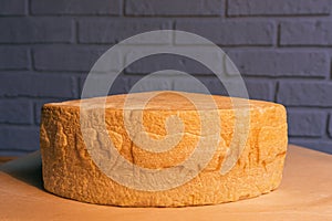 Swiss cheese on a wooden stand against a brick wall