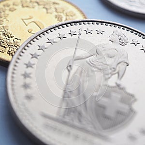 Swiss coins lie on light blue surface. 1 one frank coin closeup. Square illustration about economy or banking. Money and currency