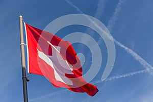 Swiss cross flag waving with crossing flight trail on blue sky background and copy space