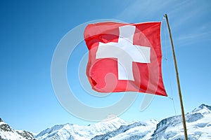 A Swiss Flag Blows in the Wind High Above the Snowy Alps.