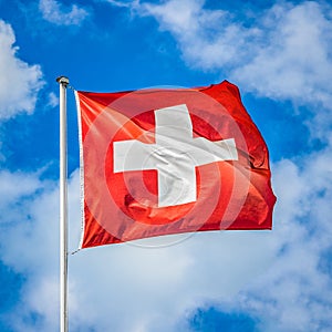 Swiss flag waving in the wind on a sunny day with blue sky and clouds