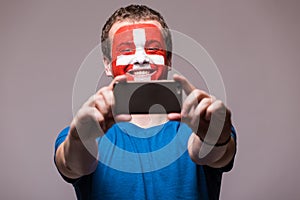 Swiss football fan take selfie photo with phone on grey background.