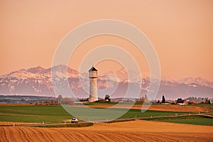 swiss landscape with snowy Alps, water tower and spring fields, image taken in canton of Vaud, Switzerland