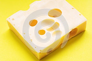 Swiss yellow cheese square chunks with holes on yellow background. Maasdam Dutch cow`s milk cheese