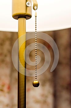 The switch of the floor lamp in the form of a chain. Stylish metal elements of lighting devices. Interior decor. Warm. Close-up.