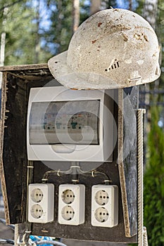 A switchboard on a construction site with sockets and an old work helmet hanging from it. Providing electricity to the