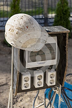 A switchboard on a construction site with sockets and an old work helmet hanging from it. Providing electricity to the