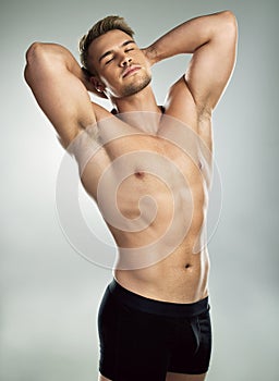 Swoon and stare all you want. Studio shot of a muscular young man posing against a grey background. photo