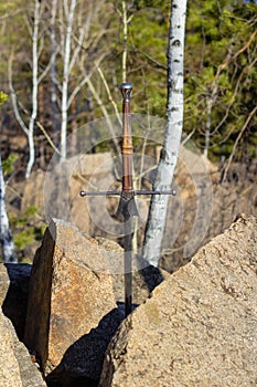 Sword in stone against the background of the forest.