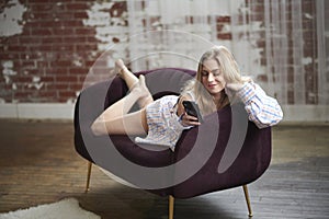 Sy blond woman in men's shirt on smartphone