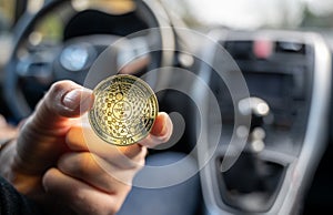 Symbol for autonomous driving. Hand holds a IOTA coin in a self driving car