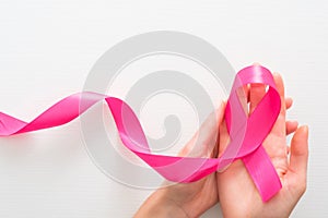 Symbol of Breast Cancer Awareness Month in October. Female hands holding pink breast cancer awareness ribbon over white background