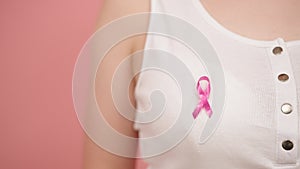 Symbol of breast cancer awareness month, pink october badge on the white shirt of unrecognizable woman