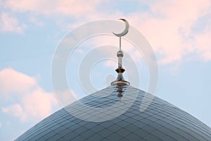 The symbol of Islam is a golden crescent moon on top of the mosque minaret. Blue evening or morning sky with clouds.