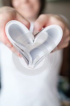 Symbol of love heart made from bent sheets of a notebook, in female hands, on a white background tee-shirt. Valentine`s