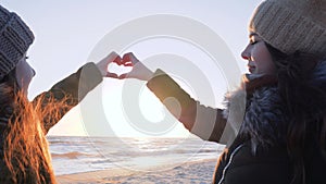 Symbol of love, homosexual couple girls making heart with hands against of sea and heaven