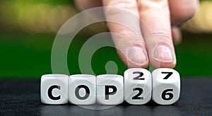 Symbol for the next climate change conference COP27. Hand turns dice and changes the expression COP26 to COP27