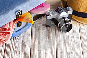 Symbol of summer holiday rest - suitcase full of objects, classic photo camera and a summer hat on wooden background