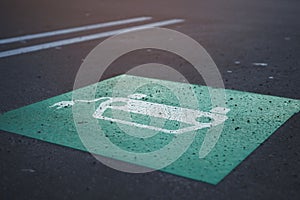symbolic graphic of a car with cable plug painted in green and white on parking lot.