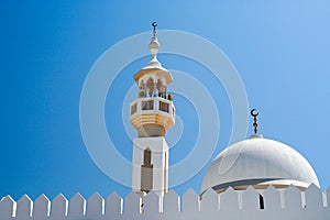 Symbols of Islam: White dome and Minarette with islamic crescent moon symbol against blue sky in Oman