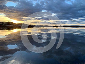 Symmetric view of the fluffy clouds reflecting on the lake water at sunset in Los Nietos