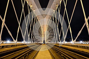 Symmetrical bridge construction in the night with bright lights, vibrat colors and rails in the center.