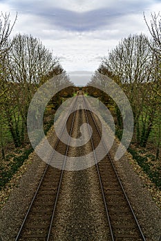 Symmetrical train tracks shot taken with view down and into the distance. Trees line both sides of the railway lines