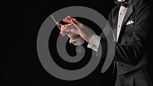 Symphony orchestra conductor wearing suit is directing musicians with movement of baton, isolated on black background