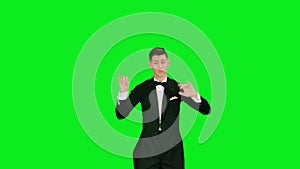 Symphony orchestra conductor wearing suit is directing musicians with movement of baton, isolated on green screen in