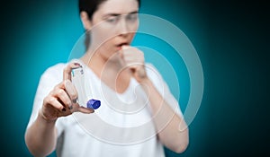 Symptoms of asthma. Portrait of a young coughing woman showing an inhaler. The background is blurred. Hand in focus. Copy space
