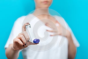 Symptoms of asthma. A woman in a blur shows an inhaler, and holds her hand to her chest. The background is blurred. In