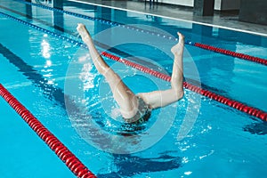 Synchronized swimming athlete trains alone in the swimming pool. Training in the water upside down. Legs peek out of the water.