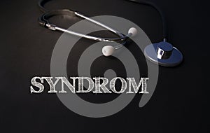 SYNDROM written in chalk on a dark background along with a stethoscope. Health care medicine concept. Top view, flat lay