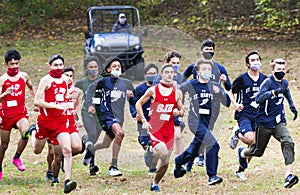 Boys running cross country race start with colf cart in back to follow them