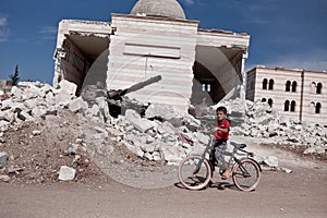 A syrian boy on bike outside of the damaged mosque in Azaz, Syria.