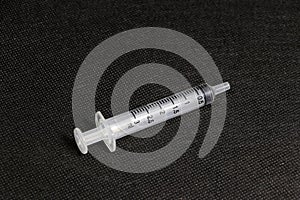 A syringe on black floor. It is simple reciprocating pump consisting of a plunger that fits tightly within a cylindrical tube