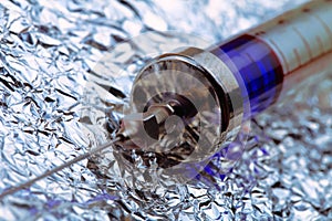 Syringe with blue content on metalpaper