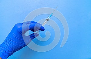 A syringe containing the coronavirus vaccine is held by a blue-gloved hand on a blue background in close-up.