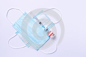 Syringe with covid-19 vaccine and two blue disposable masks on a white background. The concept of a pandemic and the