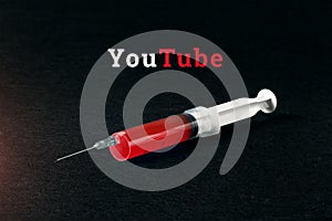 Syringe on a dark background and the word YouTube. The concept of internet addiction