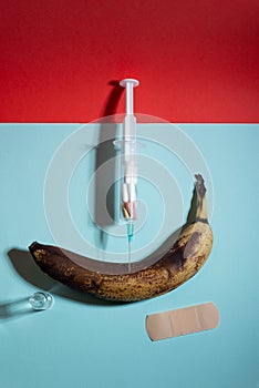 Syringe filled and banana with pills on red background