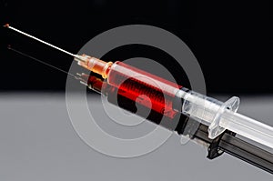 Syringe filled with a red liquid on a black acrylic background