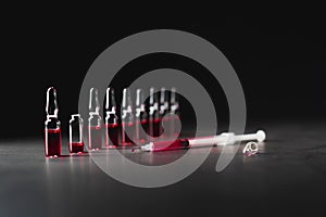 Syringe filled with red liquid from broken ampule on dark background. Low key photo. Medicine, healthcare and pharmacy