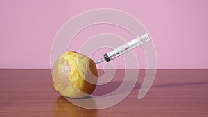 Syringe gives an injection into the rotten green apple