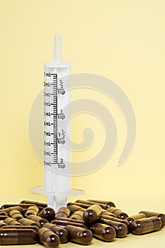 Syringe without needle and brown pills on yellow background. Medical concept
