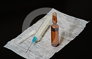 Syringe with the needle on hygienic napkin and ampule wiith medicine on black background