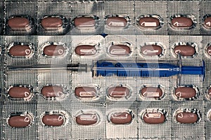 syringe with a needle lies on gray packs of brown pills